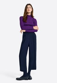 Top mov cu mânecă lungă, guler înalt, siluetă ajustată. Pantaloni largi bleumarin, cu un design pliat. Loafers negri, lustruți. Șosete texturate bleumarin.
