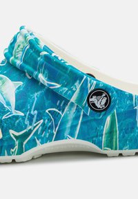 Modré a bílé dřeváky s designem marine, měkkou texturou a kulatým černým logem na popruhu.