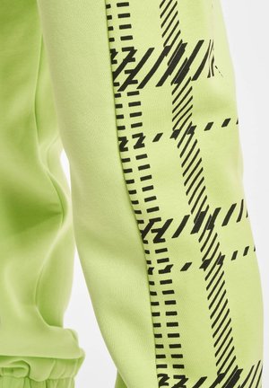 Lime žali sportiniai kelnių su juodais geometriniais raštais šonuose. Minkšta medvilnės medžiaga su lygiu paviršiumi ir elastingu juosmeniu.