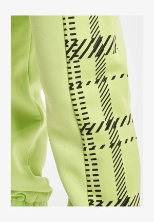Limetkově zelené tepláky s černými geometrickými vzory po stranách. Měkký bavlněný materiál s hladkou texturou a elastickým pasem.