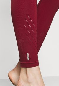 Leggings sportivi rossi con ritagli traspiranti, tessuto testurizzato e logo B-DRY sull'orlo. Design aderente.