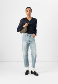 Polo a maniche lunghe navy in maglia con bottoni, jeans a vita alta azzurri, mocassini neri e una piccola borsa verde oliva.