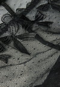 Zwarte kantstof met doorzichtige delen, bloemembroidered en satijnen lintaccenten. De textuur is delicaat en ingewikkeld met stippen.