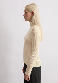 Gestrikte crèmekleurige turtleneck trui met lange mouwen, aansluitend ontwerp en een licht gebogen zoom, gecombineerd met een zwarte rok.