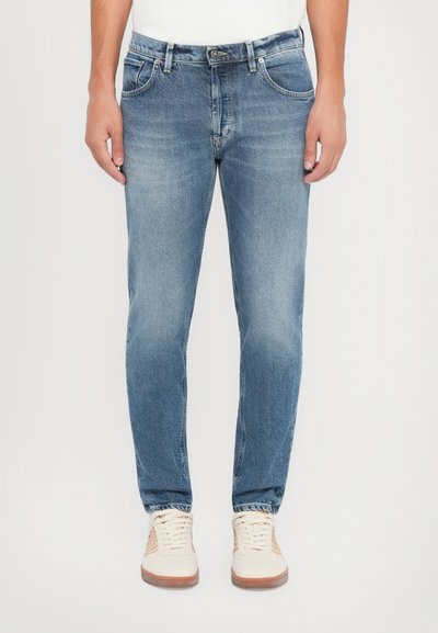 Jeans in denim azzurro chiaro con taglio dritto, design classico a cinque tasche, cuciture visibili e una leggera scoloritura. Indossati con sneakers beige.