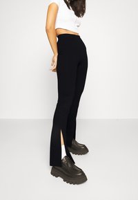 Zwarte hoge taille broek met zijsplitten en een aansluitend ontwerp. Gecombineerd met grove zwarte schoenen en witte sokken voor contrast.