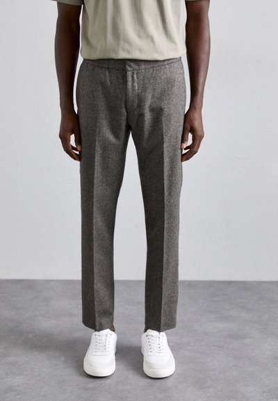 Pantalones grises texturizados con un ajuste entallado y piernas rectas, combinados con zapatillas blancas. El conjunto presenta una parte superior simple de color verde apagado.