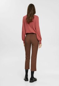 Ceglastoczerwony, długi rękaw bluzka zestawiona z brązowymi, w kratkę, krótkimi spodniami. Teksturowana tkanina z dopasowanym krojem i czarnymi butami. Gładkie tło.