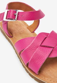 Sandalo in pelle rosa con cinturini incrociati, cinturino alla caviglia regolabile con fibbia argentata e una soletta texturizzata color tan. Suola piatta e flessibile.
