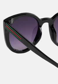 Czarne, przerośnięte okulary przeciwsłoneczne z gradientowymi fioletowymi soczewkami. Zauszniki zdobią dekoracyjne czerwone i zielone paski. Gładkie, błyszczące wykończenie.