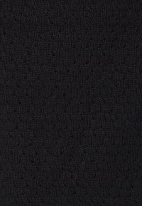 Černá pletená tkanina s texturovaným, vzdušným vzorem, který obsahuje malé otvory rovnoměrně rozložené, což vytváří jemnou hloubku a měkkost.