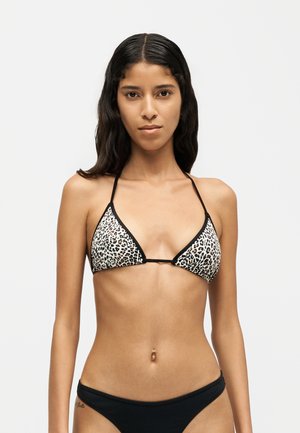 Jeune femme aux longs cheveux foncés porte un haut de bikini triangle à imprimé léopard et un bas de bikini noir uni sur un fond uni.