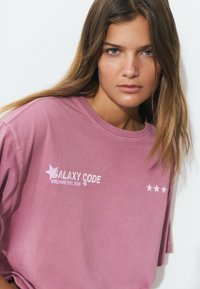 Pink cotton t-shirt features "GALAXY CODE" text and star graphic on the front. Loose fit with short sleeves and crew neck.