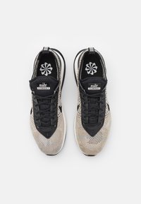 Černé a béžové tenisky Nike Flyknit s pleteným svrškem, černými tkaničkami a bílou podrážkou. Obsahují značkovou tkaničku a květinový design vnitřní stélky.