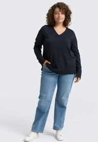 Marineblauwe V-hals trui met lange mouwen en een gestructureerde afwerking, gecombineerd met lichtblauwe recht gesneden jeans en witte sneakers.