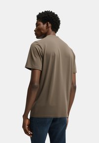 Camiseta de manga corta en color caqui con una textura suave, cuello redondo y detalles de costura sutiles, combinada con unos jeans azul oscuro.