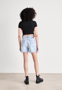 Černý krátký top s krátkými rukávy v kombinaci s vysokým pasem světlomodrých džínových šortek. Výrazné detaily zahrnují logo a krátký střih. Černé kotníkové boty.