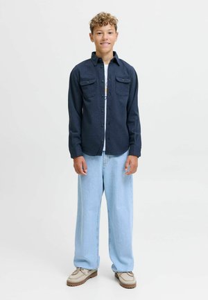 Marintröja med knäppning och två bröstfickor, ljusblå vida jeans och beige skor med strukturerad sula. En enkel vit t-shirt under.