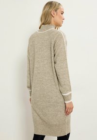 Lungo vestito a maglia beige con colletto alto, polsini a coste e strisce bianche accentate sulle spalle e sulle maniche.