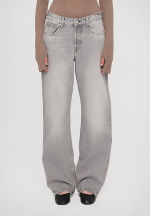 Jeans a vita alta grigi chiari con un lavaggio sbiadito, design a cinque tasche e passanti per cintura; abbinati a un top a maniche lunghe a coste e scarpe nere.