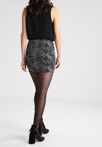 Černý bezrukávový top, vzorovaná stříbrná a černá mini sukně, průsvitné černé punčocháče s tečkami a kotníkové boty s přezkovými detaily.