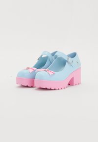 Jasnoniebieskie buty typu Mary Jane z różowymi, masywnymi obcasami, zaokrąglonymi noskami, srebrnymi akcentami i różowymi kokardkami z przodu.