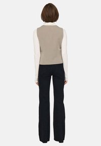 Top grigio senza maniche con un design aderente, abbinato a una camicia bianca a maniche lunghe e pantaloni neri a campana, visto da dietro.