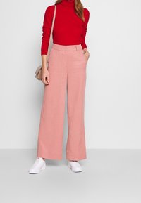 Rosa vida byxor i en texturerad tyg, med sidofickor och skräddarsydd midja. Matchas med en röd polotröja och vita sneakers.