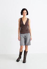 Brązowy top na ramiączkach, szare dżinsowe szorty i brązowe botki do kolan. Gładka tekstura, warstwowy design i luźny krój w stylu casual.