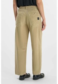 Lichtbeige corduroy broek met een gestructureerd oppervlak, voorzien van twee achterzakken en een zwart label op de rechterzak. Ontspannen pasvorm met wijde pijpen.