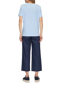 Jasnoniebieska koszulka z krótkim rękawem połączona z granatowymi szerokimi spodniami. Całość dopełniają czarne trampki z teksturowaną podeszwą.