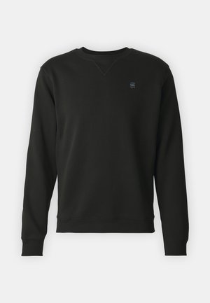 Sweatshirt preto com mangas longas, decote redondo, punhos e bainha canelados, apresentando um pequeno logótipo no lado esquerdo do peito. Textura de tecido suave.