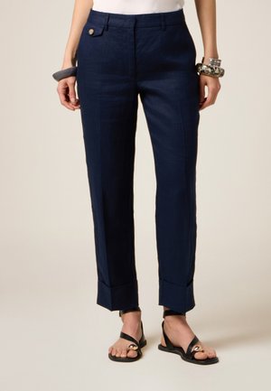 Pantaloni di lino blu navy con una vestibilità su misura, due tasche frontali e orli risvolti. Abbinati a sandali neri con dettagli in hardware dorato.