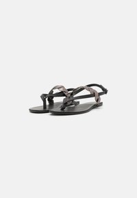 Platta sandaler i svart syntetmaterial med flätade bruna remmar, minimalistisk design och en slät matt yta.