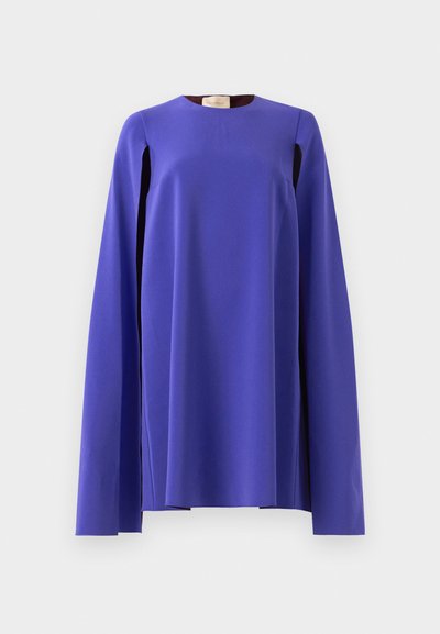 Ilga rankovė, ryškiai violetinė suknelė su plačiomis, laisvai krentančiomis rankovėmis, eksponuojama ant paprasto šviesiai pilko fono.