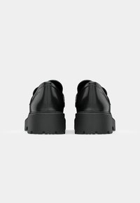 Scarpe in pelle nera con suola in gomma spessa, caratterizzate da una texture liscia e un design rotondo. Nessun marchio visibile o dettagli in metallo.