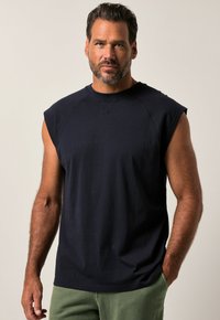 Granatowa koszulka bez rękawów z bawełny, z okrągłym dekoltem i luźnym fasonem, w połączeniu z zielonymi spodniami. Prosty i klasyczny design.