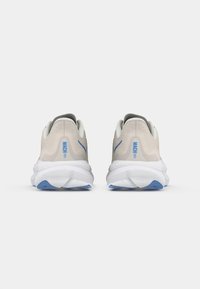 Sapatilhas de corrida Puma Mach 6 em bege e branco com detalhes em azul, mostradas por trás sobre um fundo branco simples.