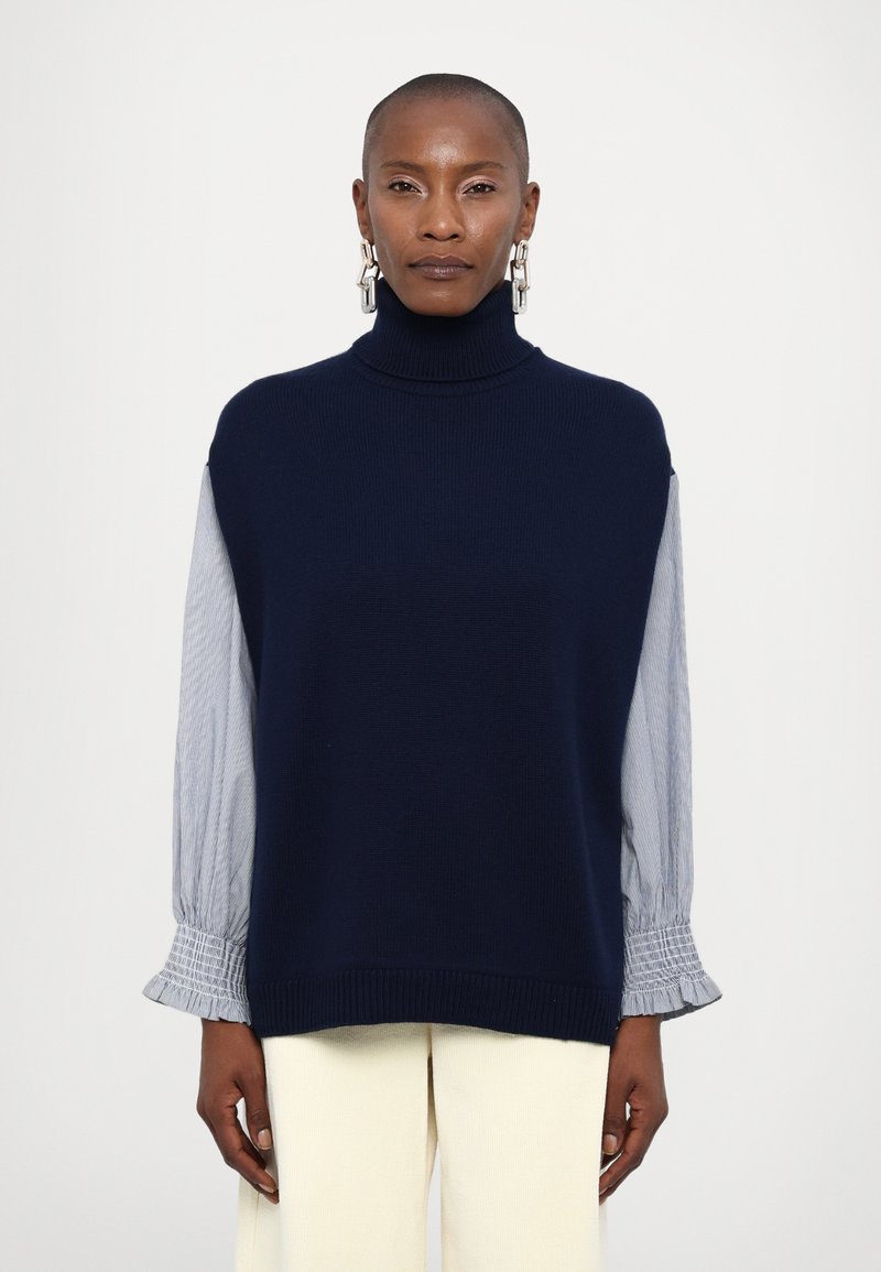 Navy knitted turtleneck sweater with gray striped sleeves, featuring gathered cuffs. Smooth texture and loose fit provide comfort.