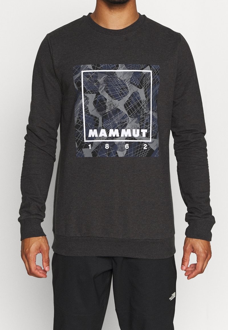 Homme portant un t-shirt à manches longues gris foncé avec un graphisme carré géométrique et le mot "MAMMUT" avec les chiffres "1862" à l'avant.