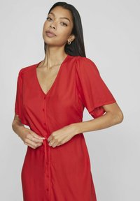 Abito rosso con bottoni, caratterizzato da maniche corte a sbuffo, scollatura a V e dettaglio a fascia in vita, realizzato in un tessuto leggero.