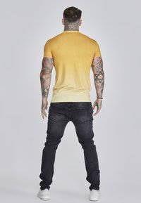 Gul gradient kortærmet t-shirt med rund hals, parret med sorte jeans. Bukserne har baglommer og en slim fit.