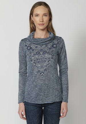 Haut à manches longues bleu marine avec col drapé, présentant une broderie complexe en argent et bleu marine sur la poitrine, fabriqué en tissu texturé.