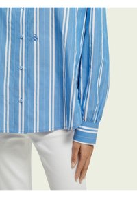 Blue and white striped button-up shirt with long sleeves, featuring a solid blue cuff and embroidered detail on the chest.