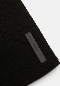 Un bonnet en tricot noir avec un tissu texturé, présentant une petite étiquette rectangulaire en cuir noir estampillée avec "ALTERNATIVE CULTURE."
