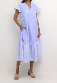 Light blue striped dress with flutter sleeves, V-neck, and a gathered hem. Features side pockets and a relaxed fit. Worn with beige block-heeled mules.