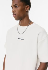 Cremefarvet oversized t-shirt lavet af bomuldsblanding, med centreret "ERROR CODE" tekst i fed sort, korte ærmer og rund halsudskæring.