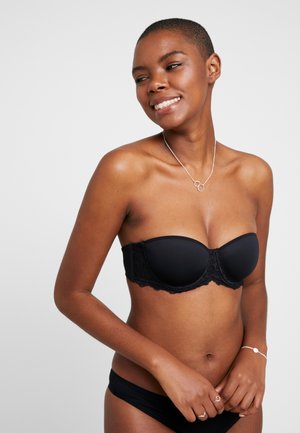 Zwarte strapless bh met gevoerde cups, kantdetails langs de band, gladde textuur, gecombineerd met zwarte bikini-broekjes. Model poseert lachend.