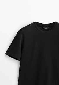 T-shirt noir à manches courtes avec col rond et coutures visibles, présenté sur un fond blanc.