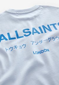 Šviesiai mėlyna medvilninė marškinėliai su ryškiu mėlynu tekstu "ALLSAINTS" ir "LONDON" anglų ir japonų kalbomis, su klasikine apvalia kaklo iškirpte.